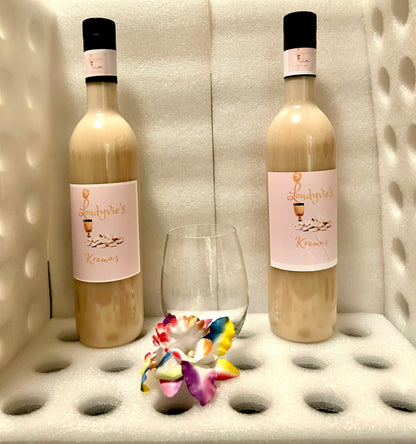 Two bottles of Loudyvie’s Kremas from Loudyvie's are positioned side by side in a white, foam-padded display, accompanied by a glass and a vibrant, multicolored orchid placed in front. The bottles feature black caps and elegant labels that evoke the rich tradition of homemade eggnog.